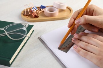 Woman drawing sketch with ruler and pencil on notebook at light table, closeup