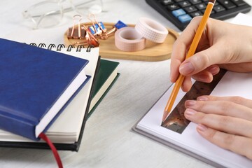 Woman drawing sketch with ruler and pencil on notebook at light table, closeup