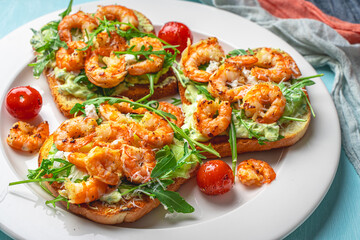 Toast with shrimp, avacado and arugula with tomatoes on a white plate on a blue background with a napkin. The concept of a healthy breakfast. Close-up.