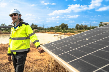 A solar technician in a high-visibility jacket and helmet stands next to a solar panel, with a...