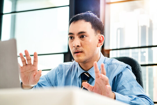 asian office man talking online meeting with shocked face. surprised office man explaining to video call business on computer device. adult business employee speaking with online conference on laptop