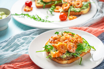 Healthy shrimp with avocado and arugula on toast for breakfast on a white plate on a light blue background.