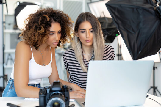 Photographer and female client editing images together on computer, reviewing portrait photos in studio