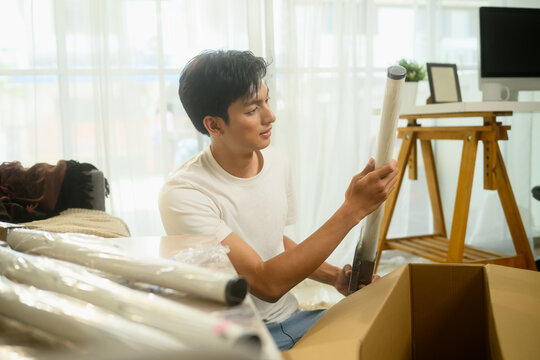 Young man unpacking furniture part, ready to assemble furniture in his living room