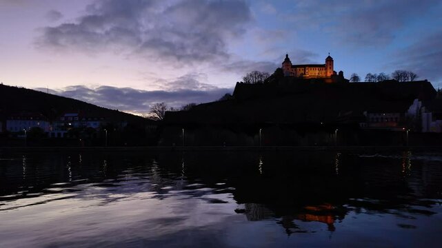 Amazing view of the Fortress Marienberg in W&uuml;rzburg, Germany. Bavarian castle with yellow evening lights in blue hour with beautiful reflections on the calm River Main in the foreground.