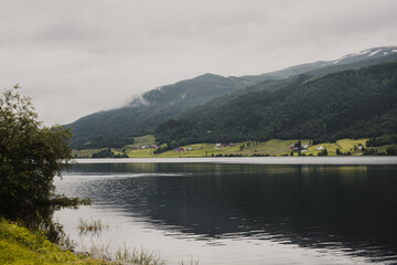 Norwegian fjord mountain landscape with a lake in the foreground and wooden houses on the shore. Overcast autumn day.