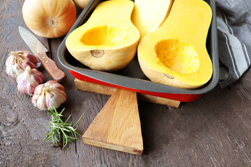Halved butternut squash pumpkin on wood cutting board. Knife and kitchen towel on dark background.