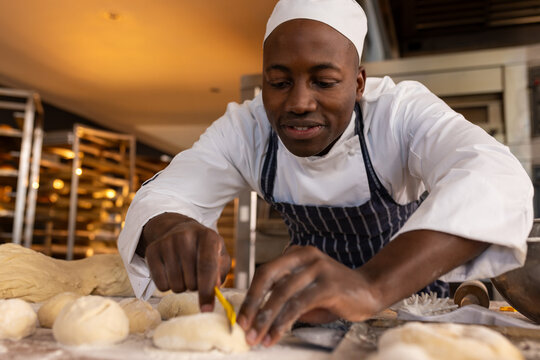 African American baker shaping dough with precision in busy bakery kitchen