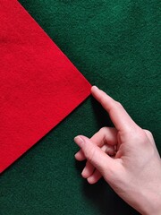 A human hand gently touches the corner of a red felt sheet placed on a green felt surface,...