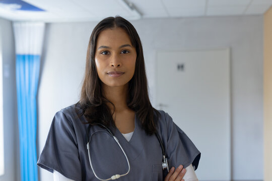 Confident female doctor in scrubs standing in hospital corridor with stethoscope