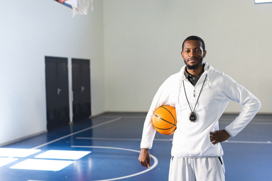 Basketball coach holding ball confidently in gym, ready for training session, copy space