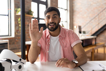 Smiling man in casual shirt waving during video call in modern office