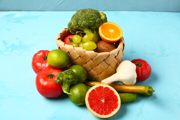 Wicker basket with different fresh fruits and vegetables on blue background