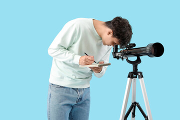 Young man with telescope and notebook on blue background © Pixel-Shot