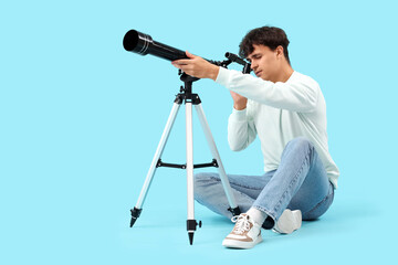 Young man looking at stars through telescope on blue background © Pixel-Shot