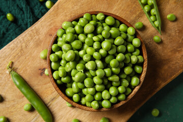 Bowl and wooden board with fresh green peas on color background, closeup