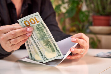 A woman puts a stack of dollar bills in an envelope