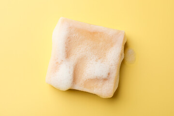 Soap bar with foam on yellow background, top view