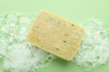 Soap bar with foam on green background, top view