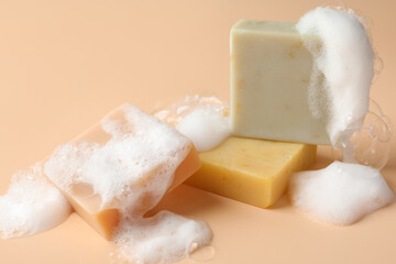 Soap bars with foam on beige background, closeup