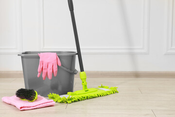 Microfiber mop, brush, bucket and gloves on wooden floor near white wall. Space for text © New Africa