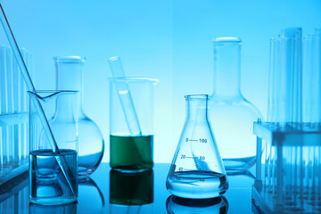 Laboratory glassware with liquid on mirror surface against light blue background