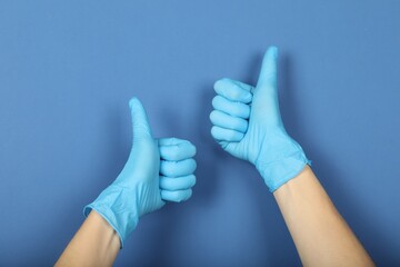 Doctor in medical gloves showing thumbs up on blue background, closeup