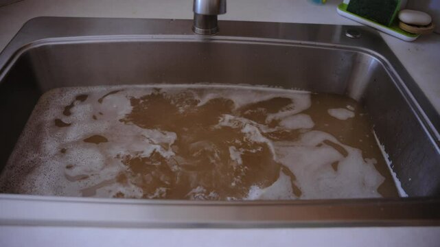 Stainless steel sink filled with murky, brown water, a drainage issue, clogged pipes, or contaminated water supply. Dirty water is coming back to the sink.