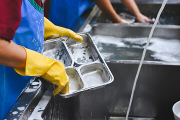 A woman is washing a stainless steel food tray.