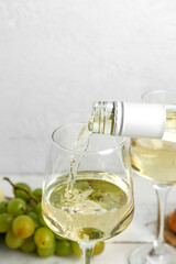 White wine pouring into glass on light background, closeup
