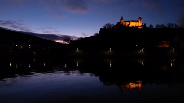 Amazing time lapse of the Fortress Marienberg in W&uuml;rzburg, Germany. Bavarian castle with yellow evening lights in blue hour with beautiful reflections on the River Main in the foreground.