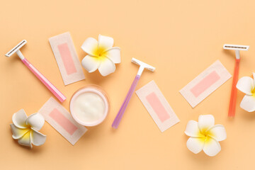 Safety razors with wax strips, jar of cream and beautiful flowers on orange background