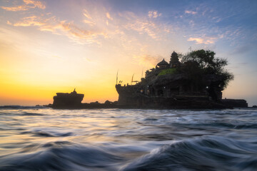 As golden hour nears, a magical light illuminates a historic sea Tanah Lot Temple, surrounded by gentle waves and vibrant clouds, creating a tranquil, reflective scene, Bali, Indonesia