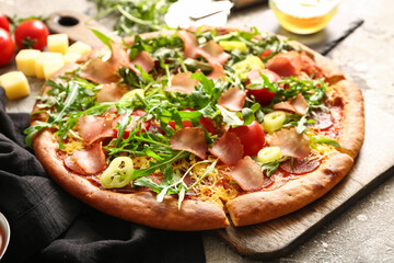 Wooden board of delicious pizza with tomatoes and arugula on grey background
