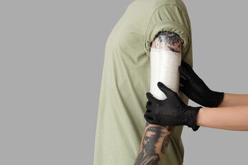 Tattoo master in gloves applying protective film cover over fresh tattoo on man's arm against grey...