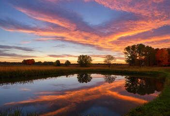 Fototapeta premium A reflective farm pond, the still water mirroring the vivid colors of an autumn sky just before sunset.