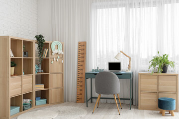 Modern children's room interior with comfortable workspace, laptop and wooden stadiometer