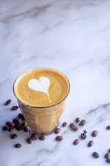 glass of latte coffee with coffee beans on white marble table.