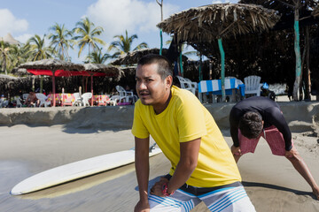 latin surf instructor and two men beginner surfers try to stand up on surfboard on lesson at beach...
