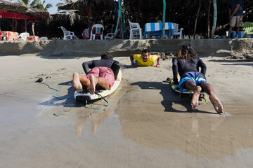 latin surf instructor and two men beginner surfers try to stand up on surfboard on lesson at beach...