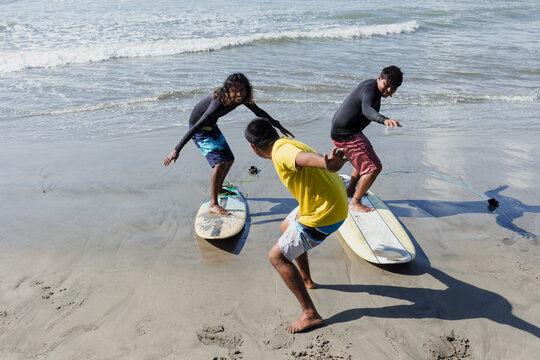 latin surf instructor and two men beginner surfers try to stand up on surfboard on lesson at beach in Acapulco Mexico Latin America, Hispanic people surfing in summer sport activity - Powered by Adobe