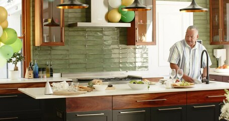 Happy senior diverse couple cleaning and washing up in kitchen decorated with balloons - Powered by Adobe