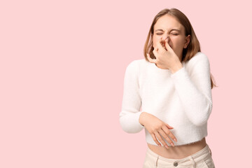 Young woman feeling disgusting smell on pink background