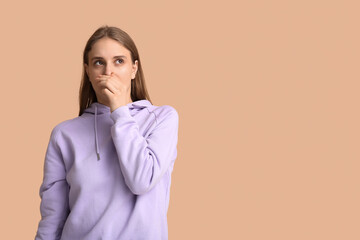 Young woman feeling disgusting smell on beige background