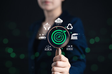 Sustainable energy and environmental conservation concepts. Woman holds magnifying glass focusing on green target icon sustainability symbols, renewable energy, eco goals, recycling, carbon footprint,