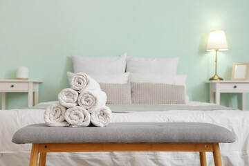 Rolled clean white towels on bedside soft bench in bedroom
