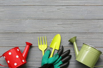 Shovel, gardening fork and watering cans on grey wooden background. Top view
