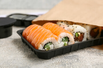 Plastic plate with tasty sushi rolls and paper bag on light grunge background, closeup. Delivery concept