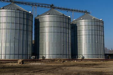 Three towering silos dominate the landscape, showcasing a blend of industrial design and agricultural functionality, set against a bright midday sky