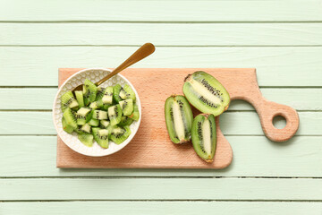 Board and bowl with cut fresh kiwi on green wooden background